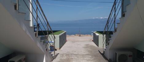 A narrow pathway leading to a beach with a clear view of the sea and mountains in the distance.