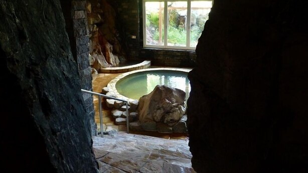Habitación de paredes de piedra con un jacuzzi, una ventana y techo de madera.
