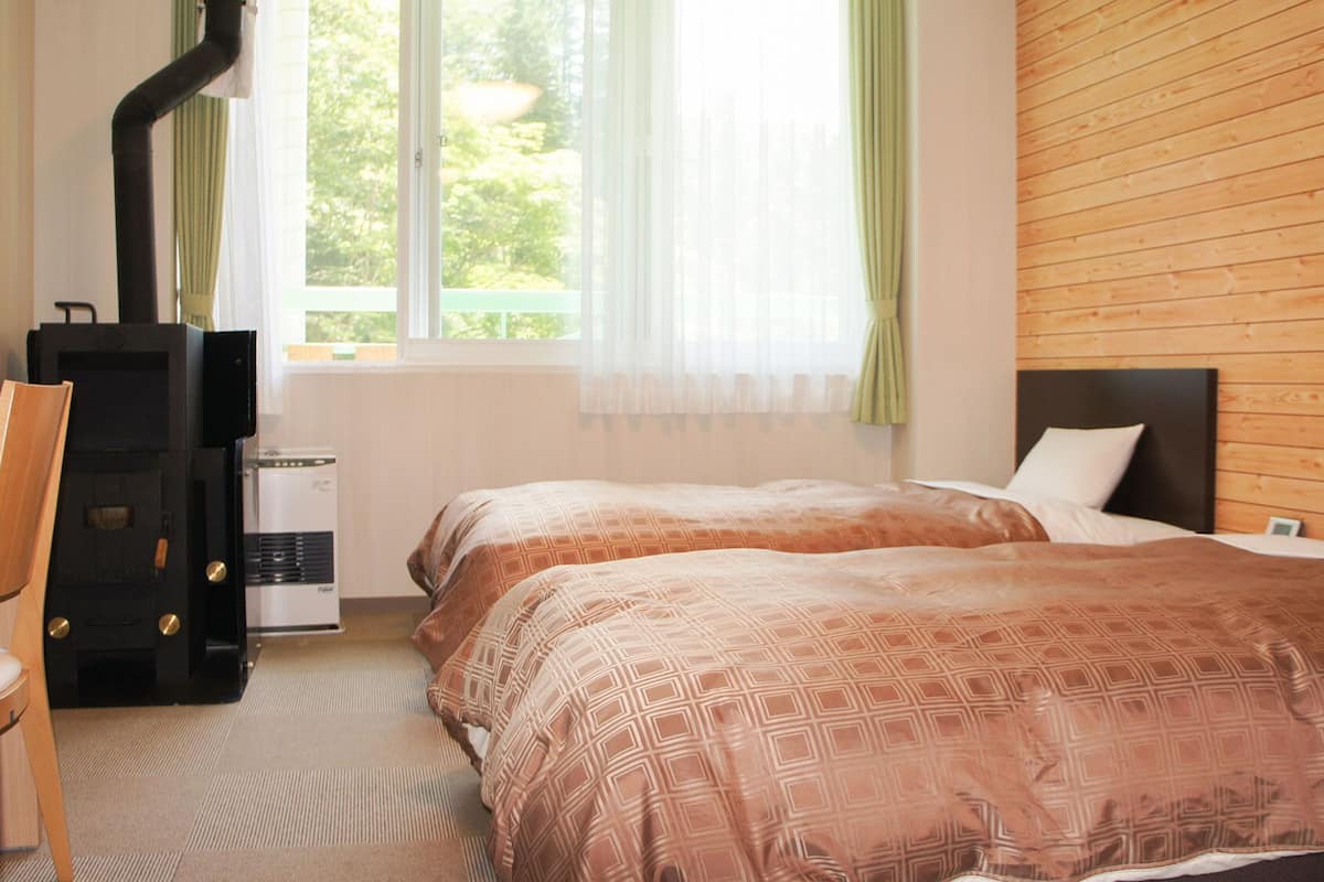 A hotel room with two beds, a desk, a chair, a heater, and a window with curtains.
