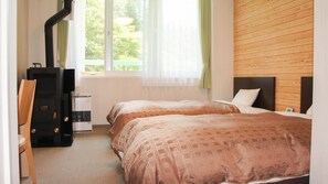 A hotel room with two beds, a desk, a chair, a heater, and a window with curtains.