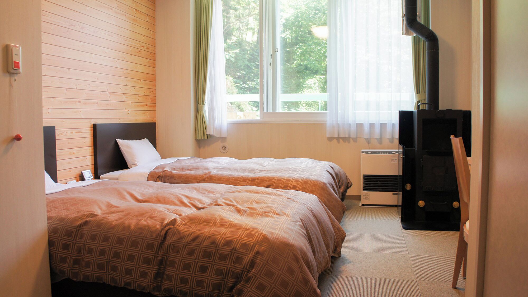 A hotel room with two beds, a TV, a heater, and a window with curtains.