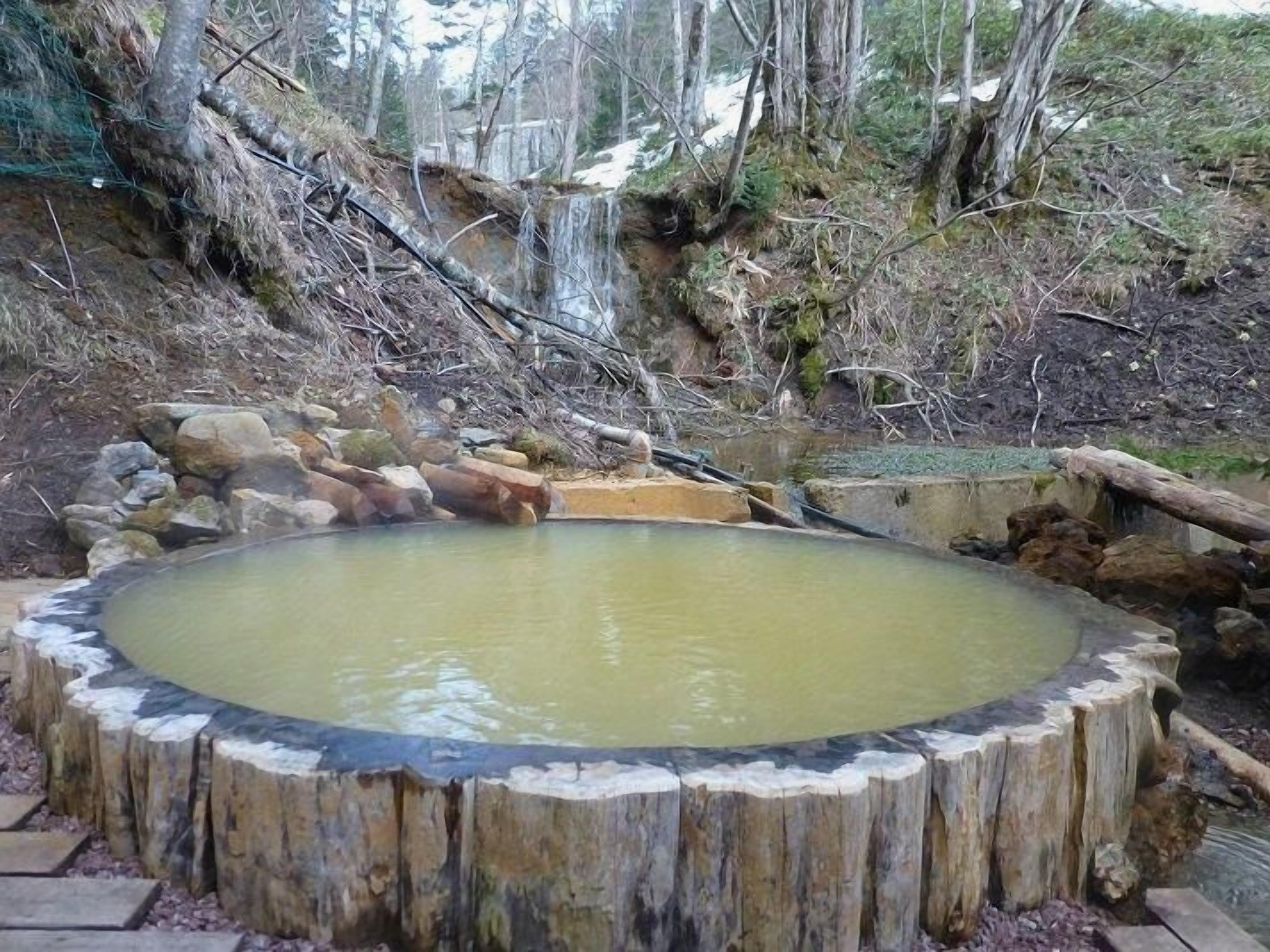 A circular wooden structure with a water feature, surrounded by natural terrain and trees.