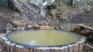 A circular wooden structure with a water feature, surrounded by natural terrain and trees.