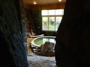 A stone-walled room with a stone bathtub, a wooden ceiling, and a window.