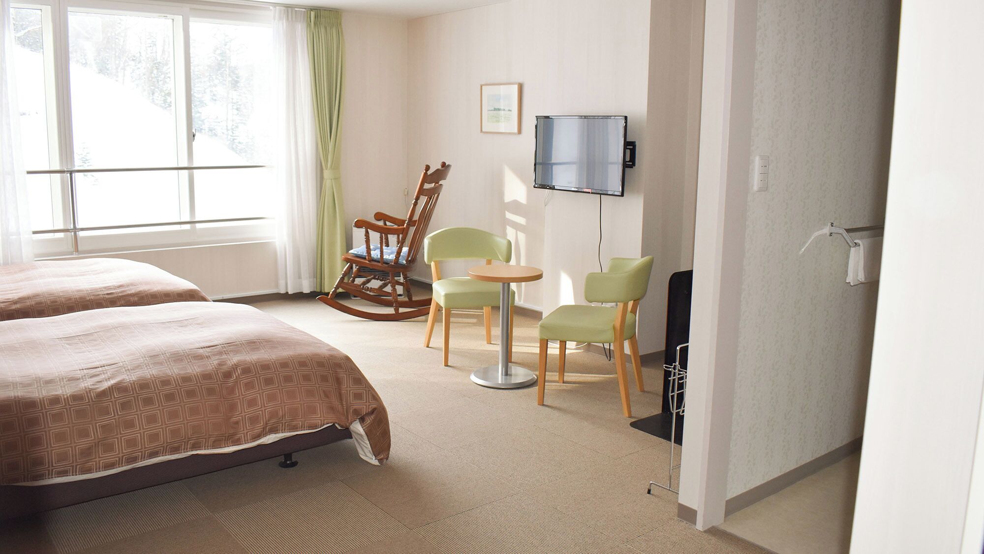 A hotel room with two beds, a rocking chair, a small table, and a TV.