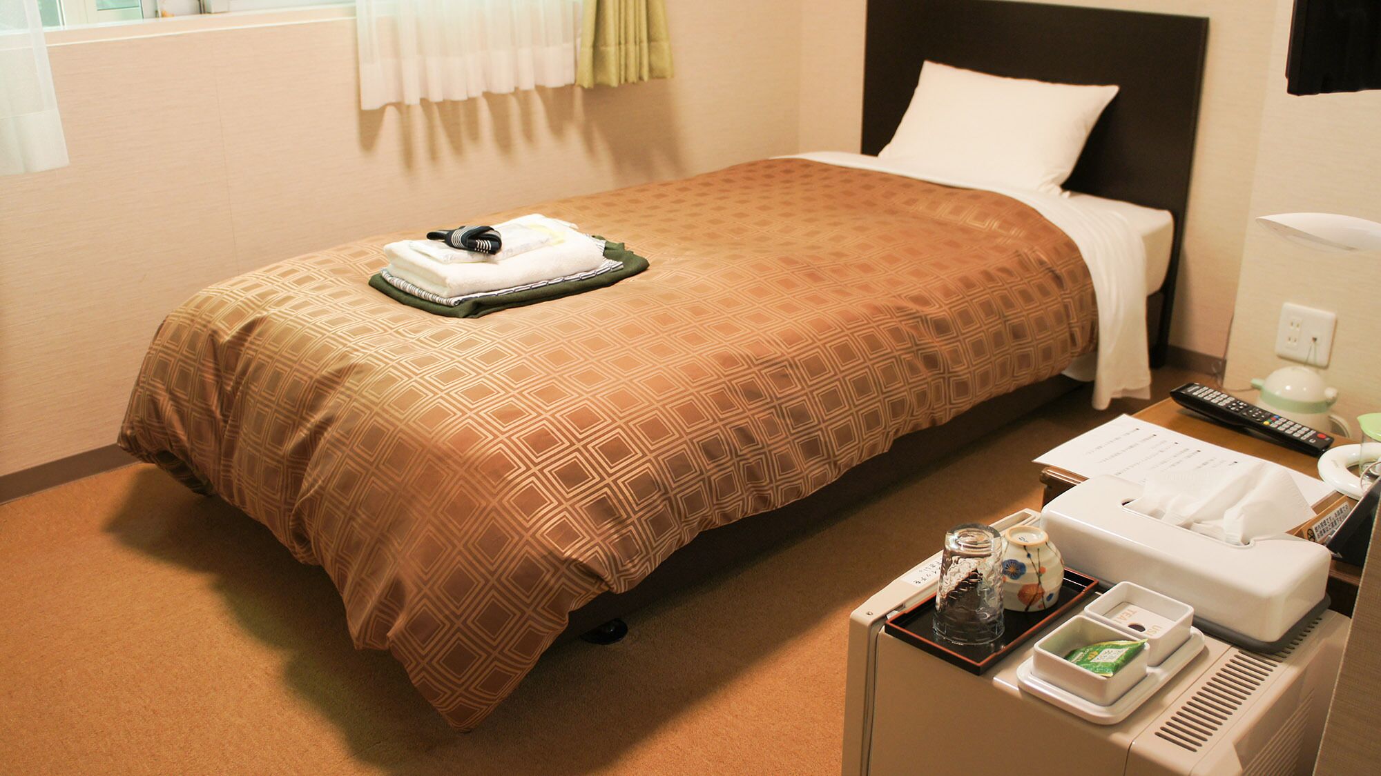 Habitación de hotel con cama, mesita de noche con teléfono, control remoto y bandeja con artículos de aseo.