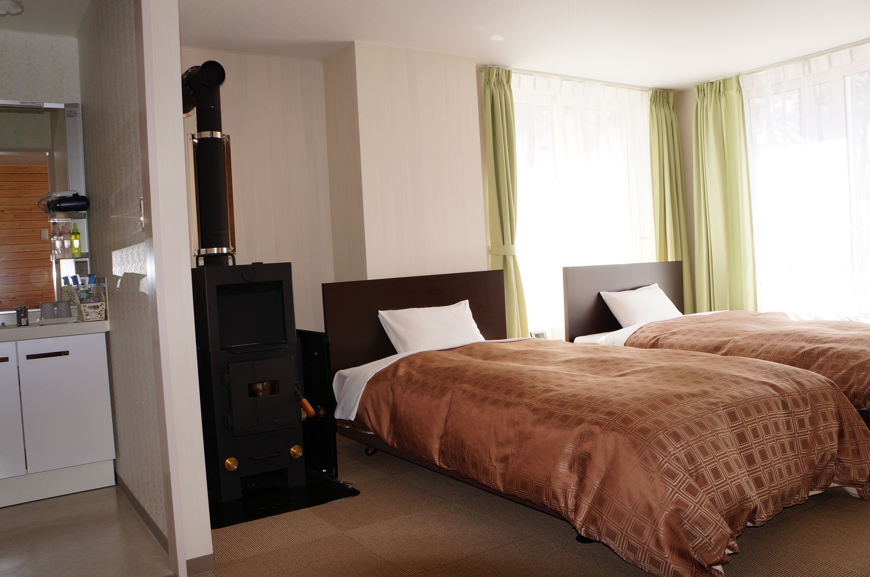 A hotel room with two beds, a kitchenette, and a wood-burning stove.