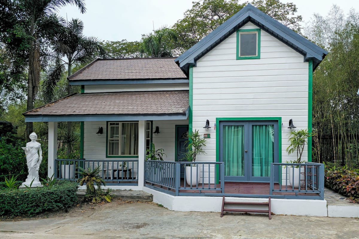 Une maison à deux étages avec un porche, des volets verts et une statue.