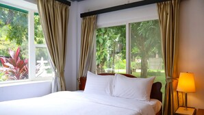 A neatly made bed with white linens, a bedside lamp, and curtains on a window overlooking greenery. - Dara Express by Angkor Green Gardens (Siem Reap)