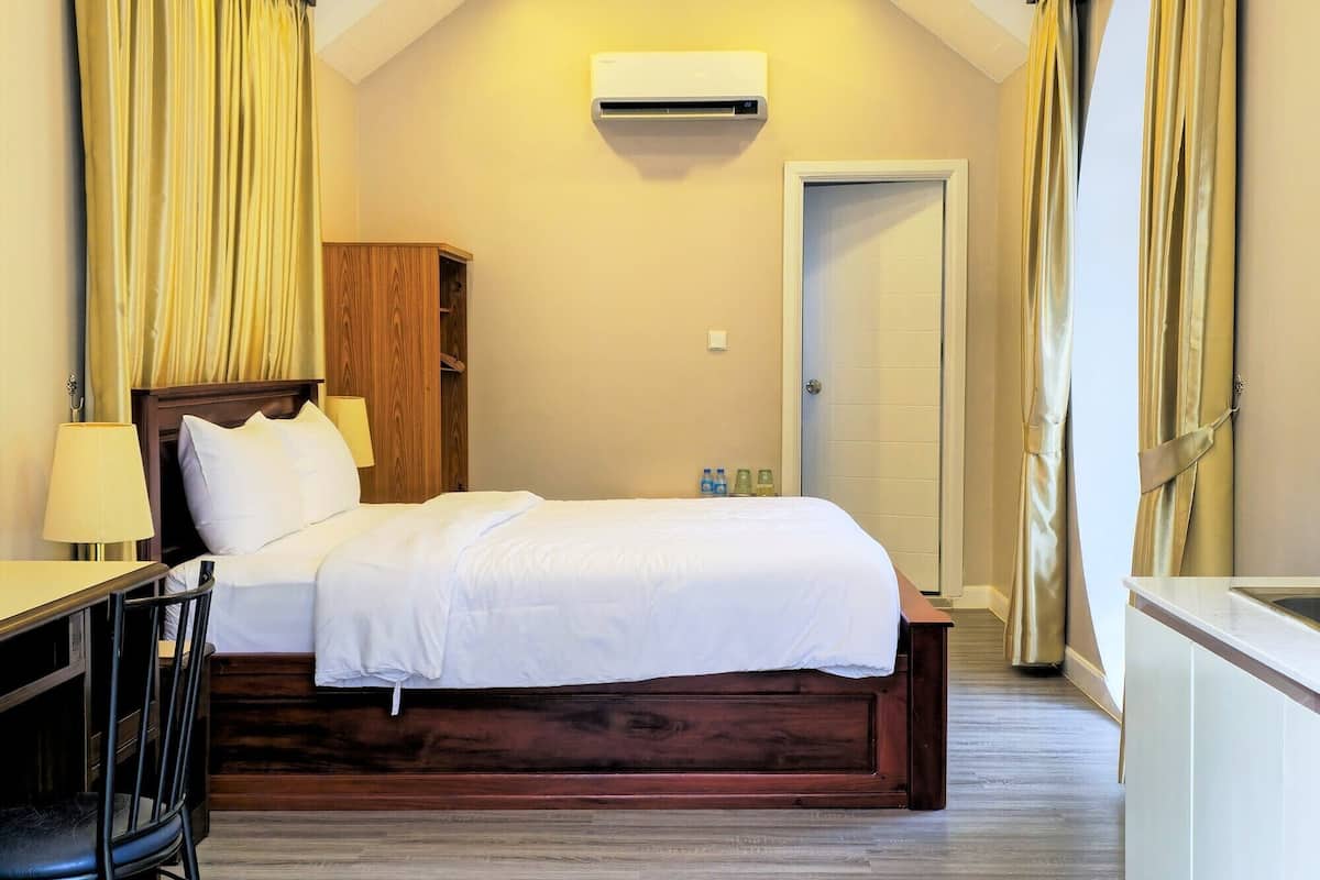Une chambre avec un lit, un bureau et une chaise. Il y a un climatiseur fixé au mur et une porte à l’arrière-plan.