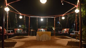 An outdoor seating area with a covered table and swing chairs, surrounded by hanging lights. - Jayshrea Meadows Tadoba Tiger Resort (Bhadravathi)