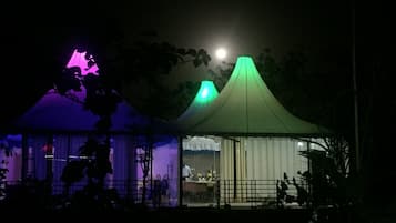 Una tienda de campaña con techo verde, una habitación iluminada de morado y una luna de fondo.