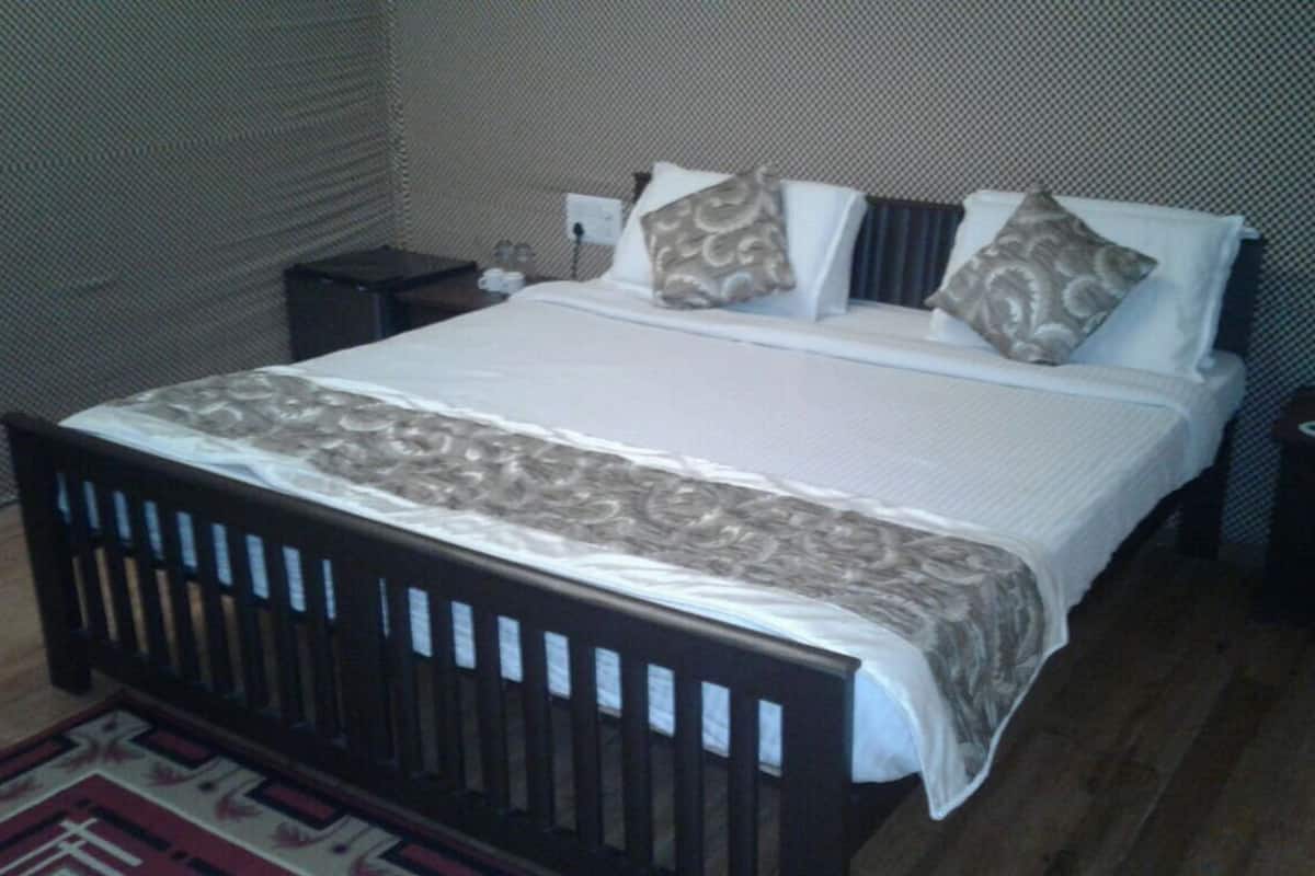 Quarto de hotel padrão com uma cama de solteiro, mesa de cabeceira e tomada na parede.