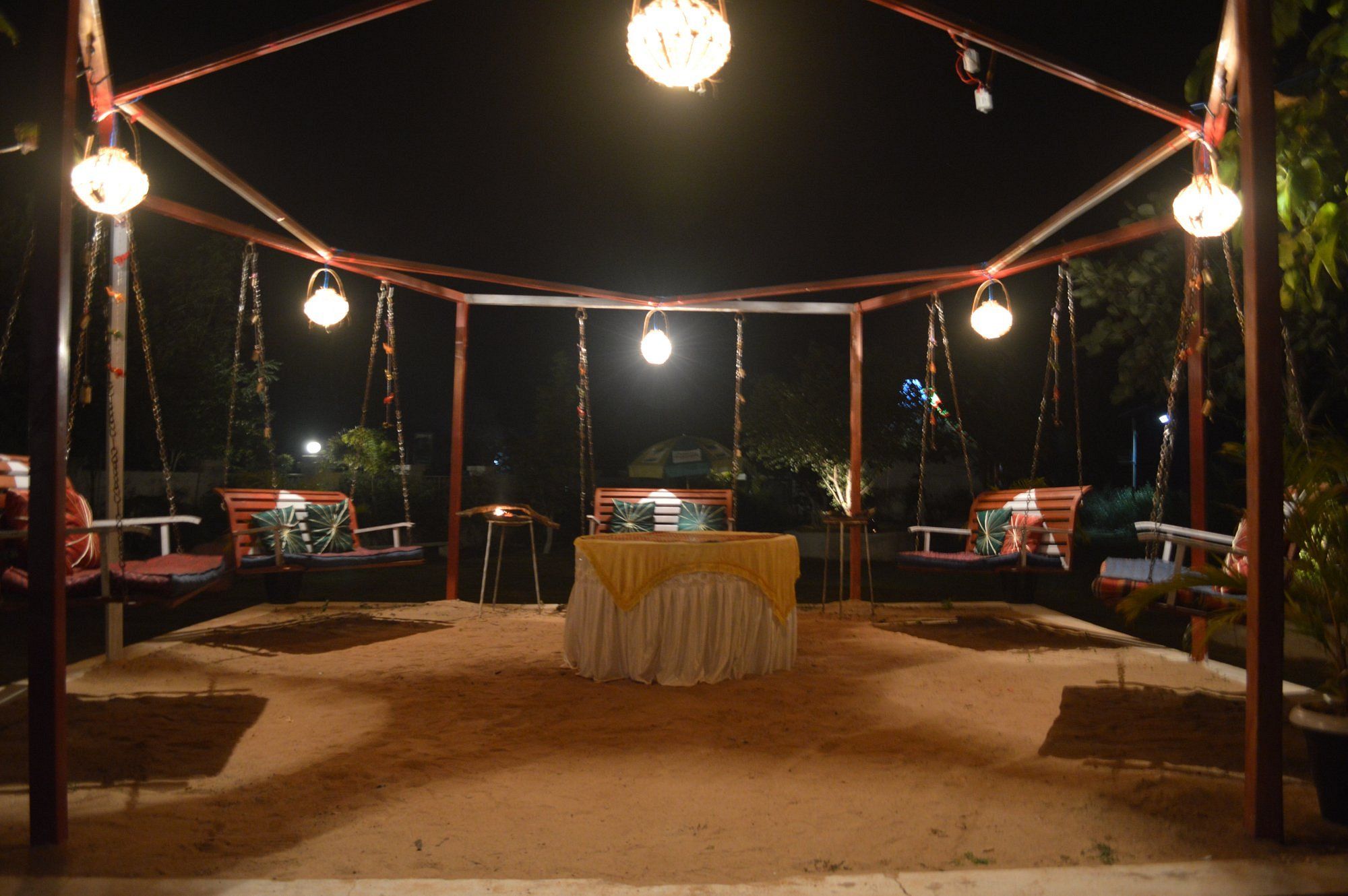 An outdoor seating area with a covered table and swing chairs, surrounded by hanging lights.