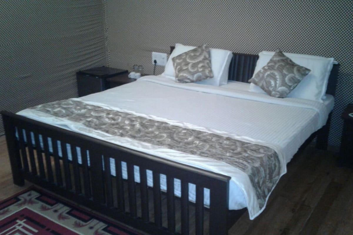 A standard hotel room with a single bed, a bedside table, a nightstand, and a power outlet on the wall.