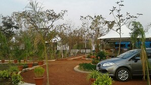 A parking area with a car, surrounded by potted plants and trees. - Jayshrea Meadows Tadoba Tiger Resort (Bhadravathi)