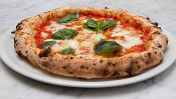 A pizza with a thick crust, topped with cheese and basil leaves, on a white plate.