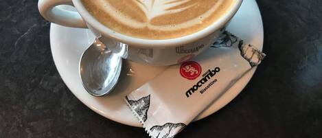 A cup of coffee with latte art on a saucer, a spoon, and a packet of biscotti.