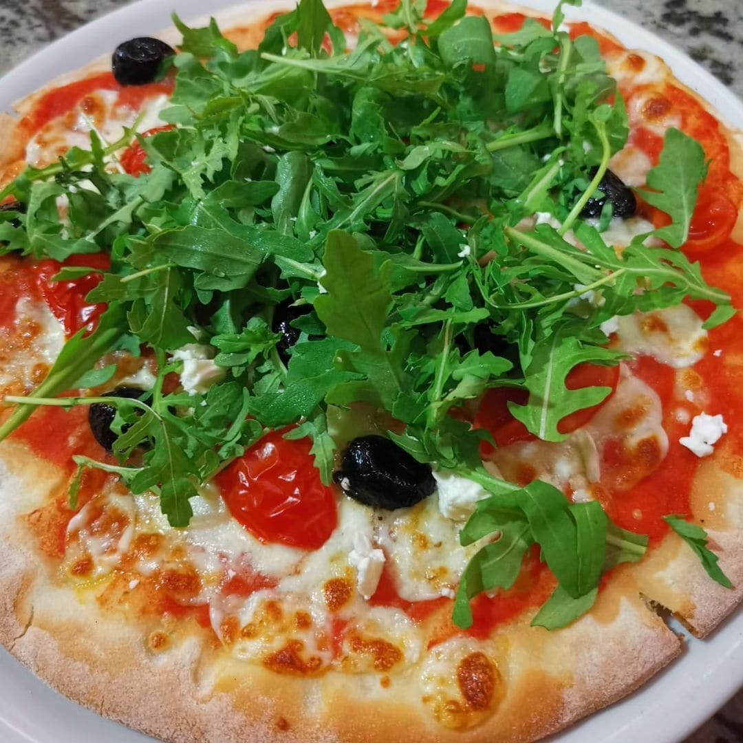 A pizza topped with greens, tomatoes, and olives.
