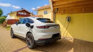 A white Porsche Cayenne parked in front of a yellow building with a wooden roof. - Hotel JMS Holiday Allgäu (Oberreute)