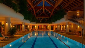 An indoor swimming pool with a tiled floor, surrounded by lounge chairs and a staircase. - Hotel JMS Holiday Allgäu (Oberreute)