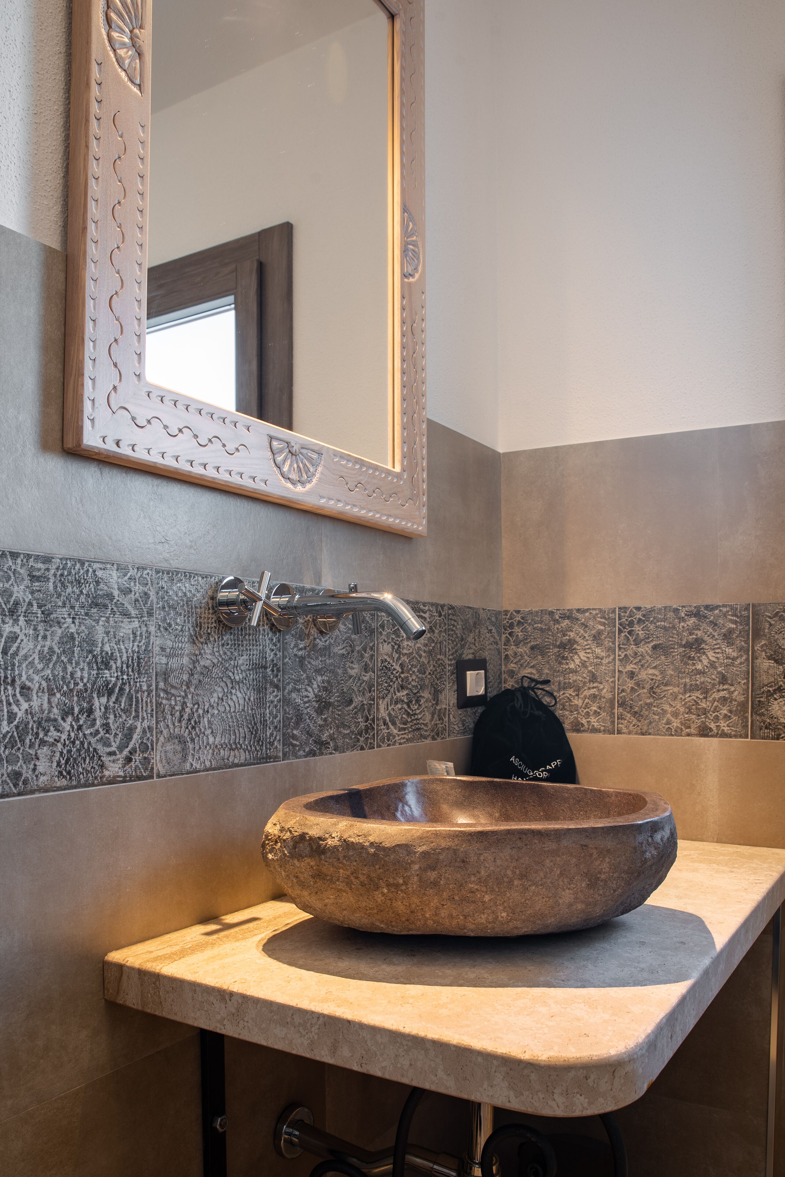 Un bagno con lavabo in pietra, uno specchio e una parete rivestita di piastrelle.