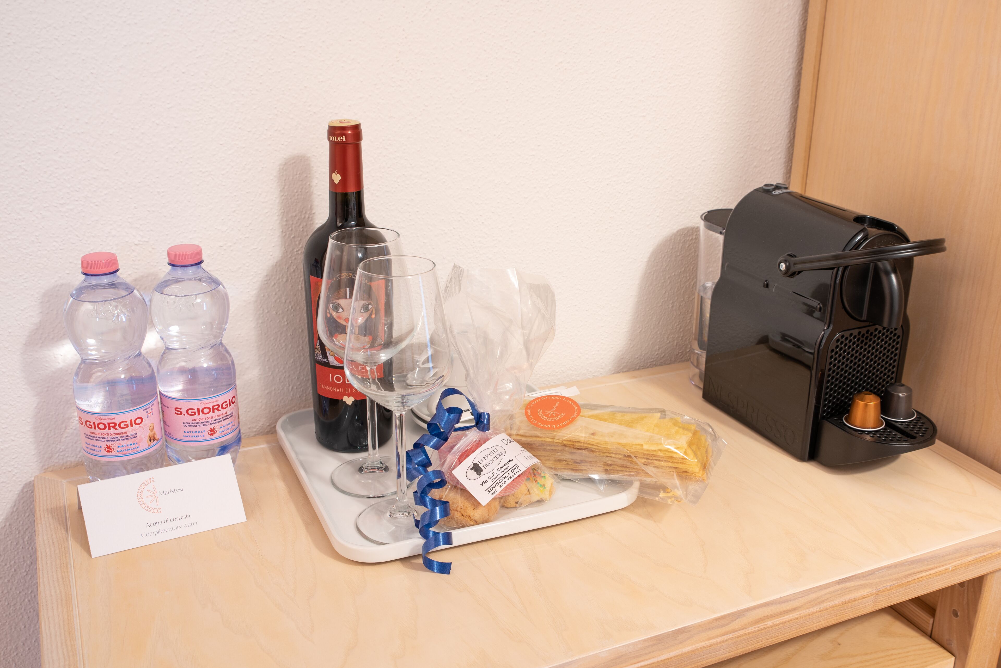 Una mesa con una botella de vino, dos botellas de agua, una copa, una bandeja con comida y una cafetera.