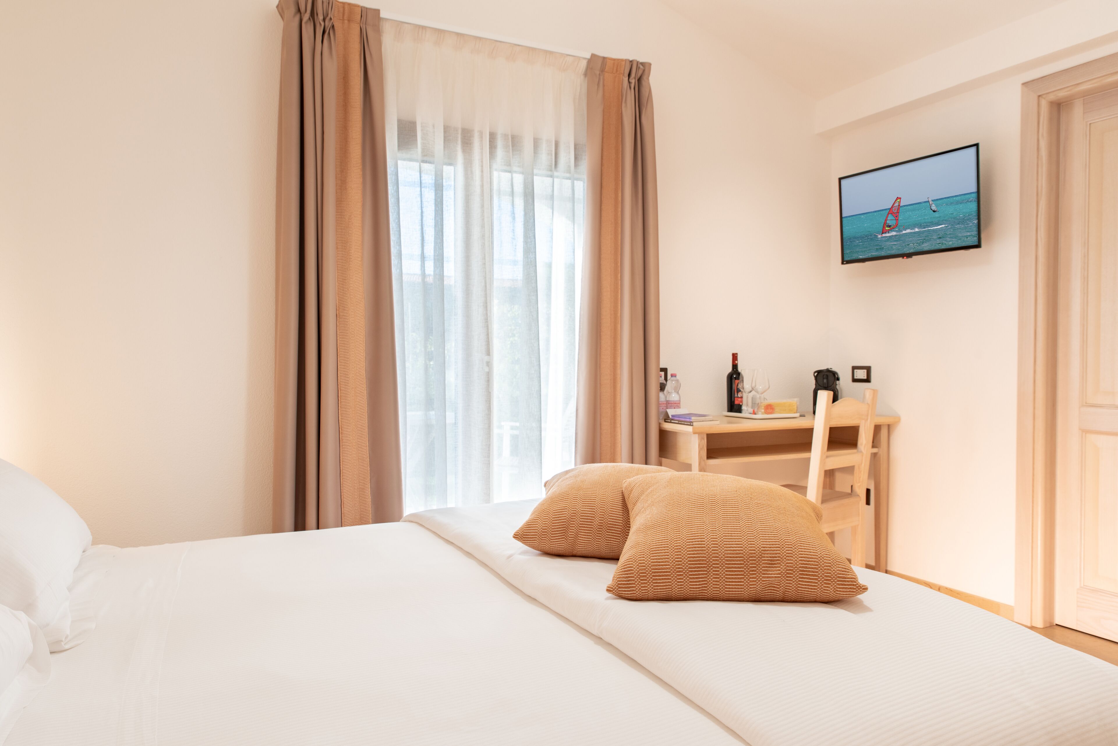Ein Hotelzimmer mit Bett, Schreibtisch, Stuhl, Fernseher und einem fensterbepflanzten Fenster.