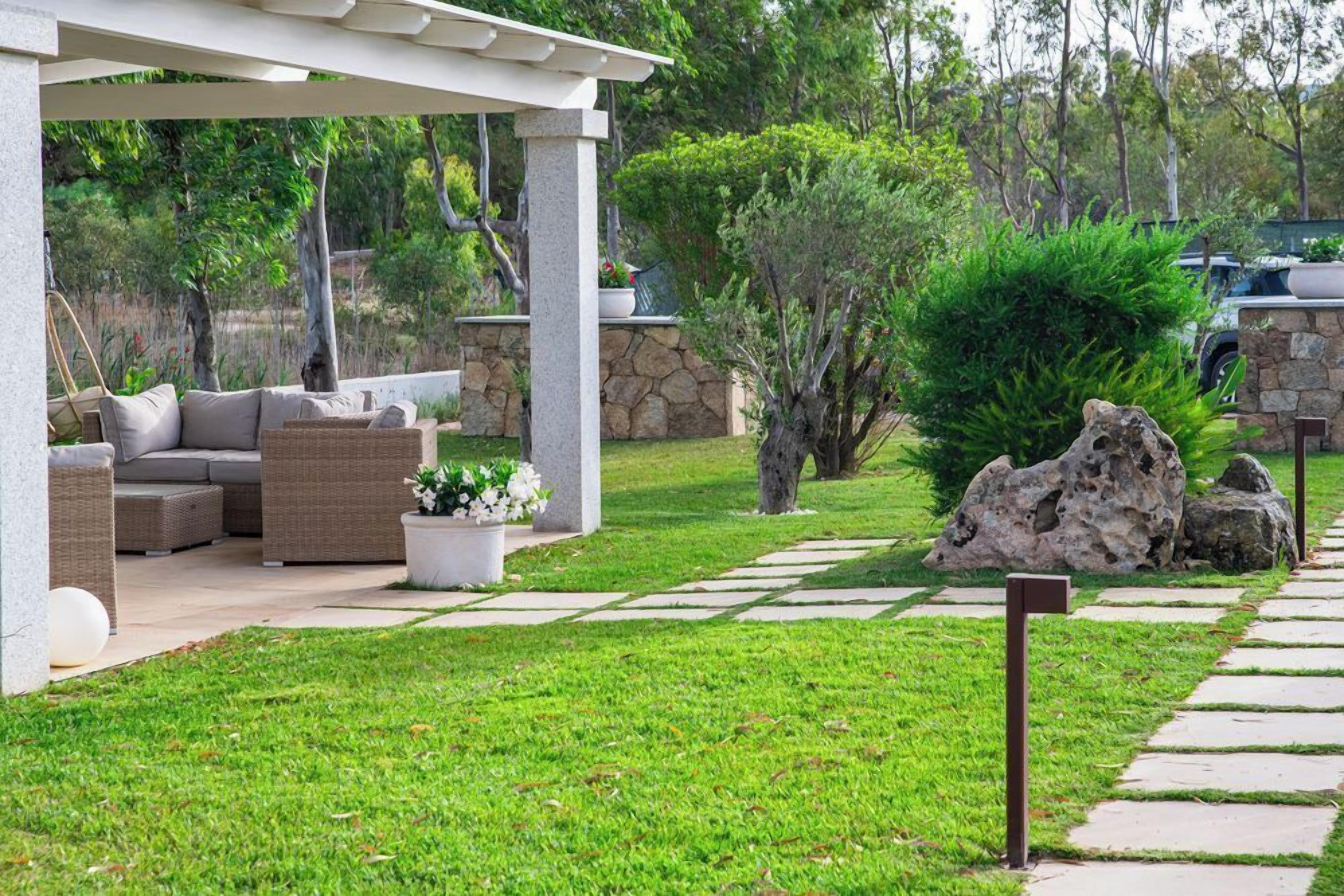 A covered outdoor seating area with wicker furniture and a stone wall backdrop.