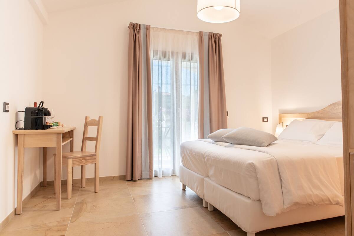 A bedroom with a bed, a desk with a chair, and a window with curtains.