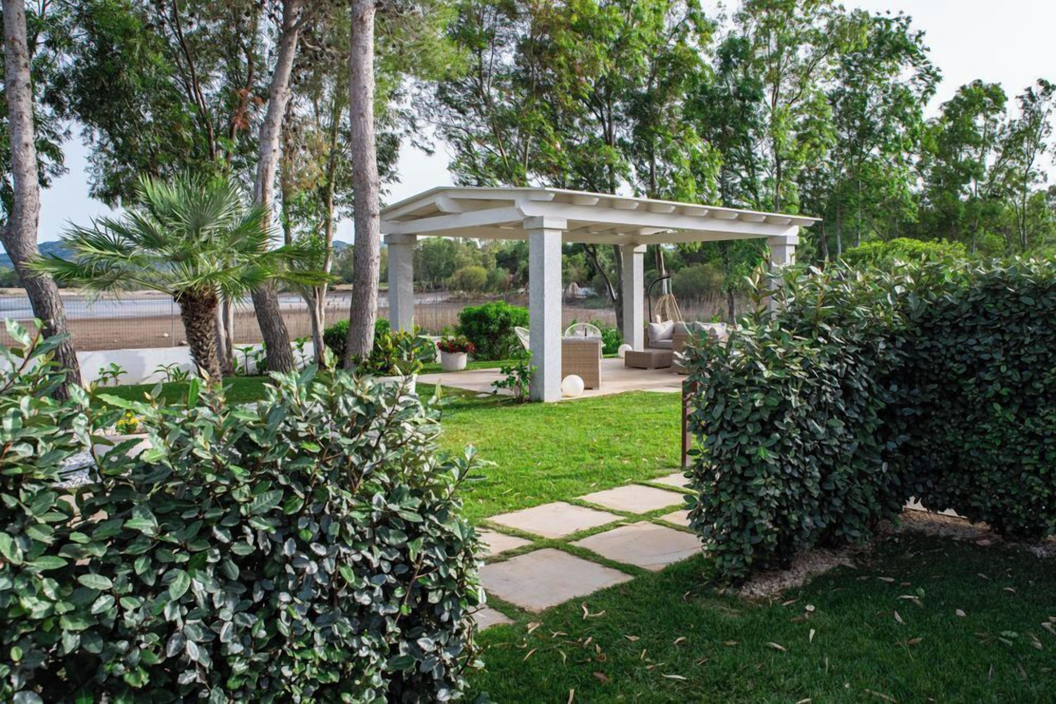 Un patio cubierto con un pérgola, rodeado de setos cuidados y un césped.