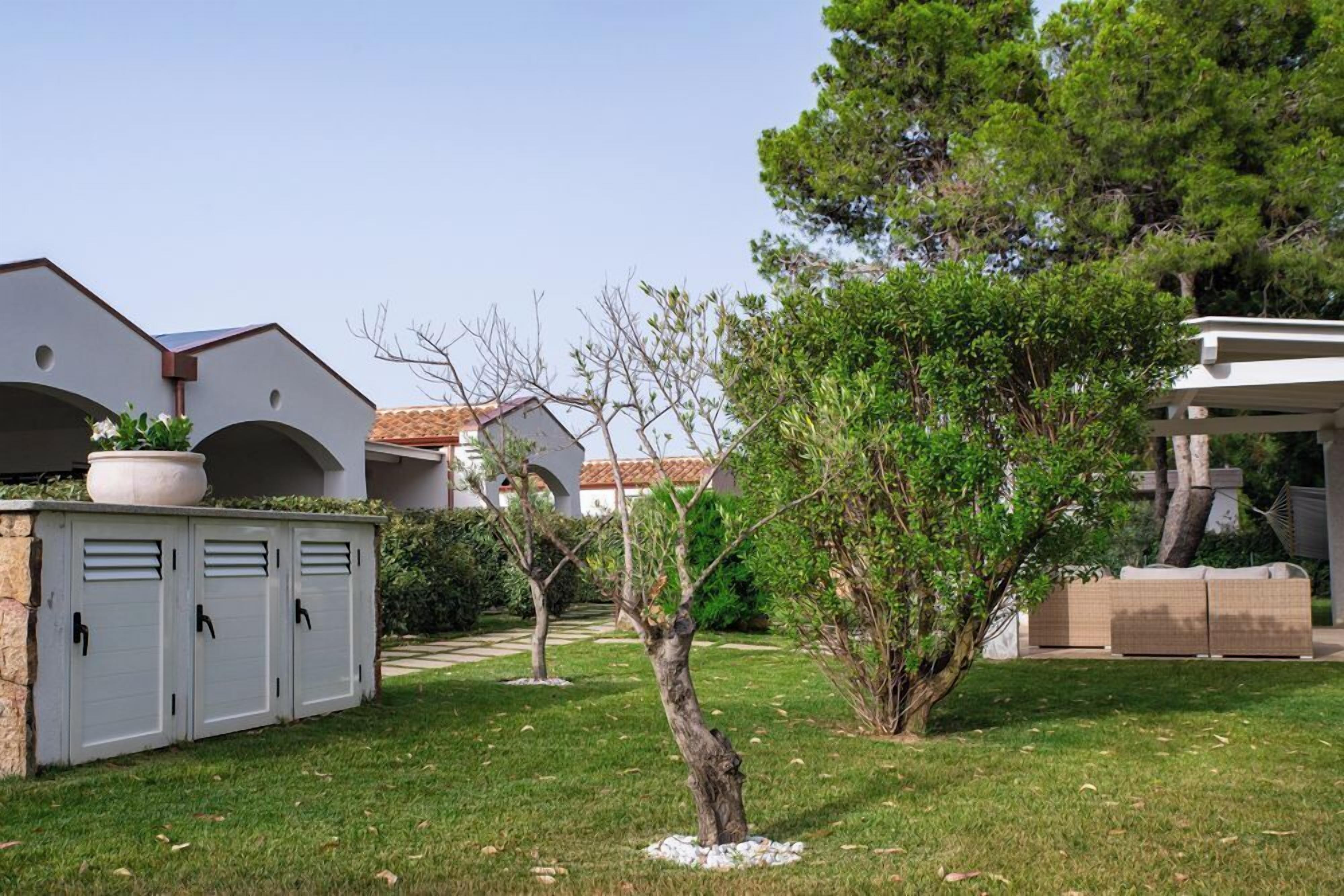 A courtyard with a white building, a covered seating area, and a small tree.