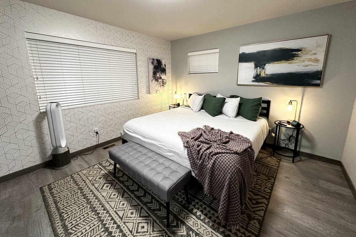 Ein modernes Schlafzimmer mit einem großen Bett, einer Bank, gemusterten Teppichen und Kunstwerken an den Wänden.