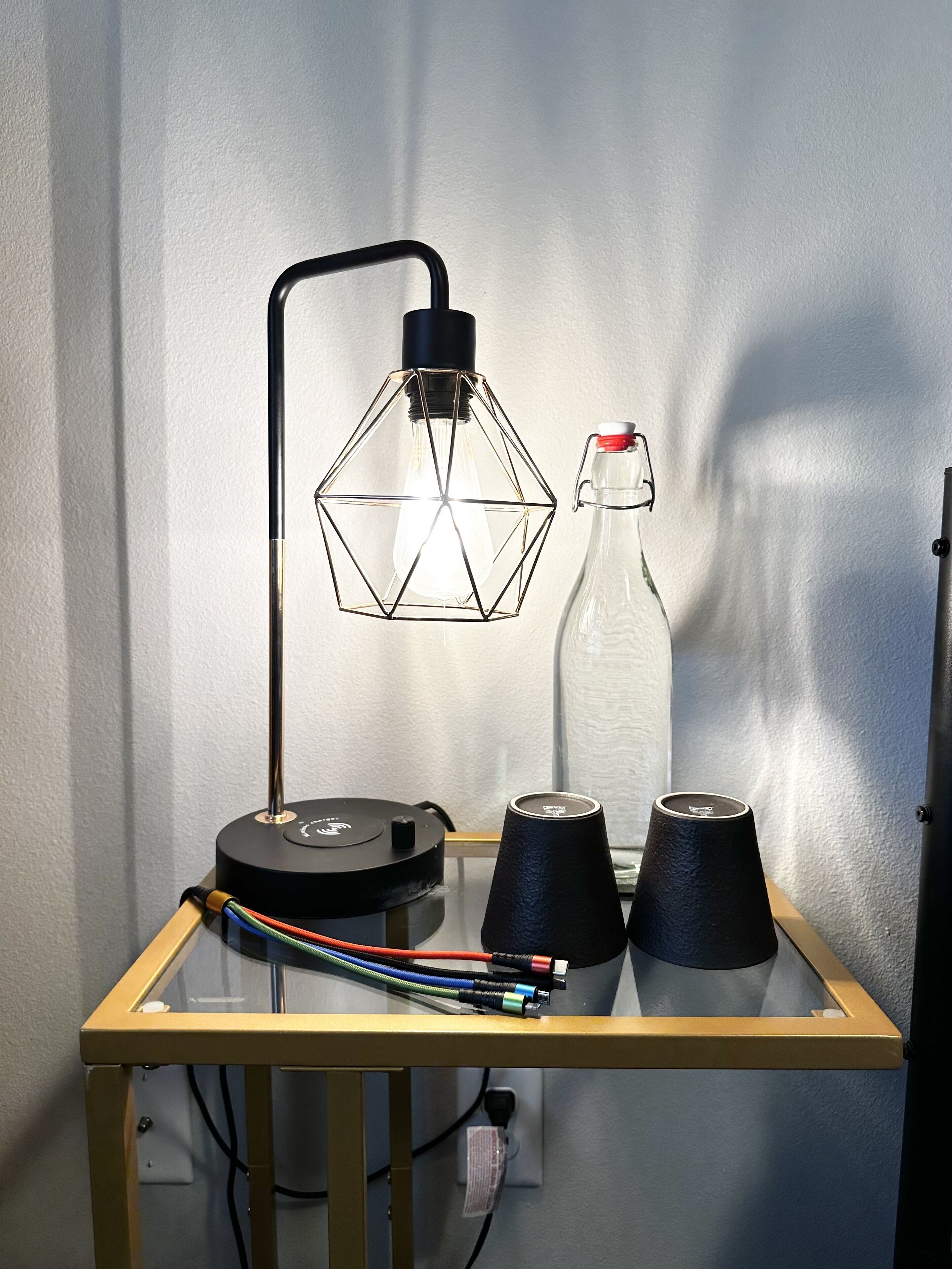 Un tavolo con una lampada, una bottiglia di vetro e due coni neri.