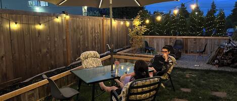 Eine Terrasse im Freien mit Tisch und Stühlen, einem großen Sonnenschirm und Lichterketten.