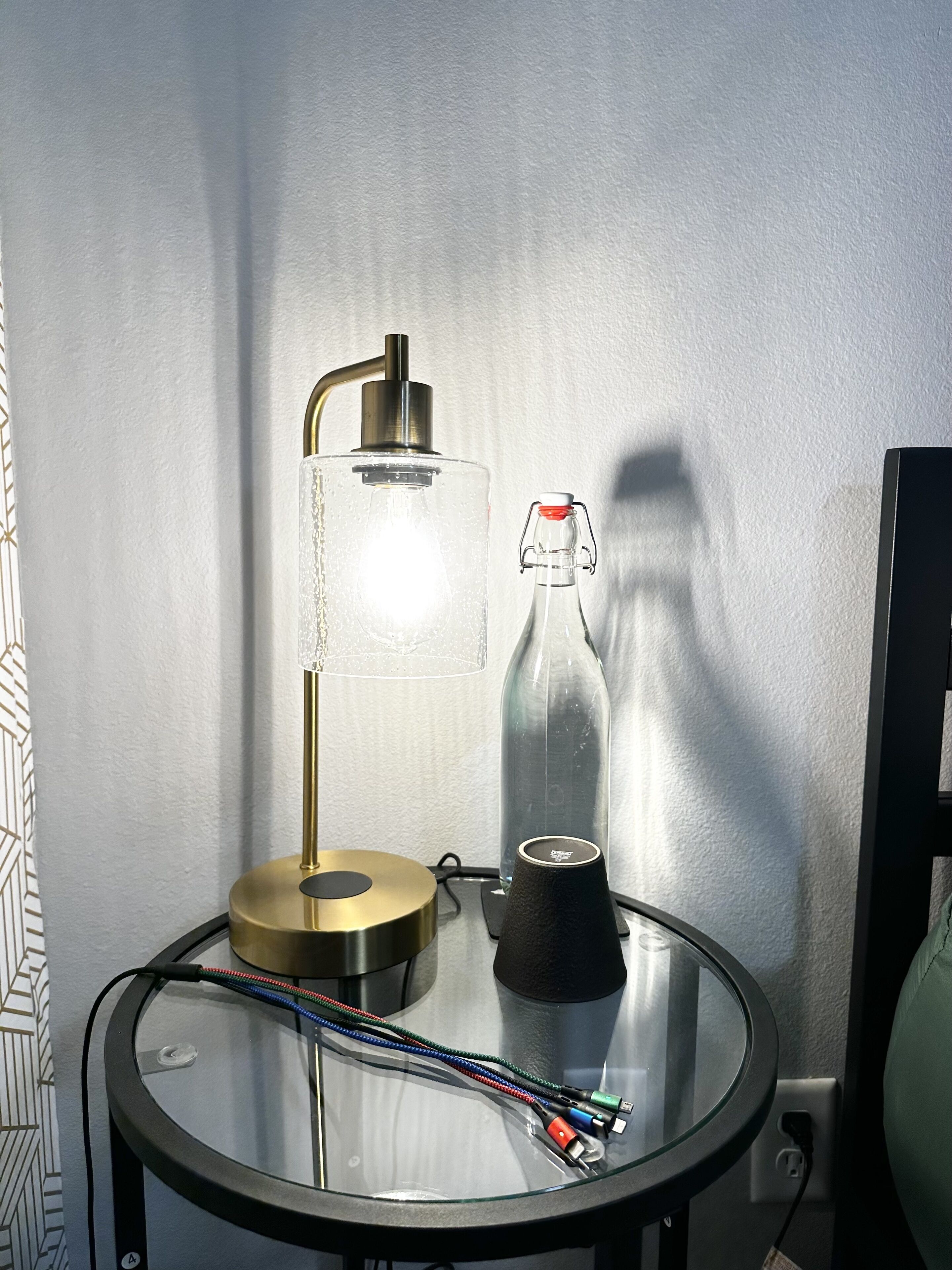 A glass table with a lamp, a bottle, and some cables.
