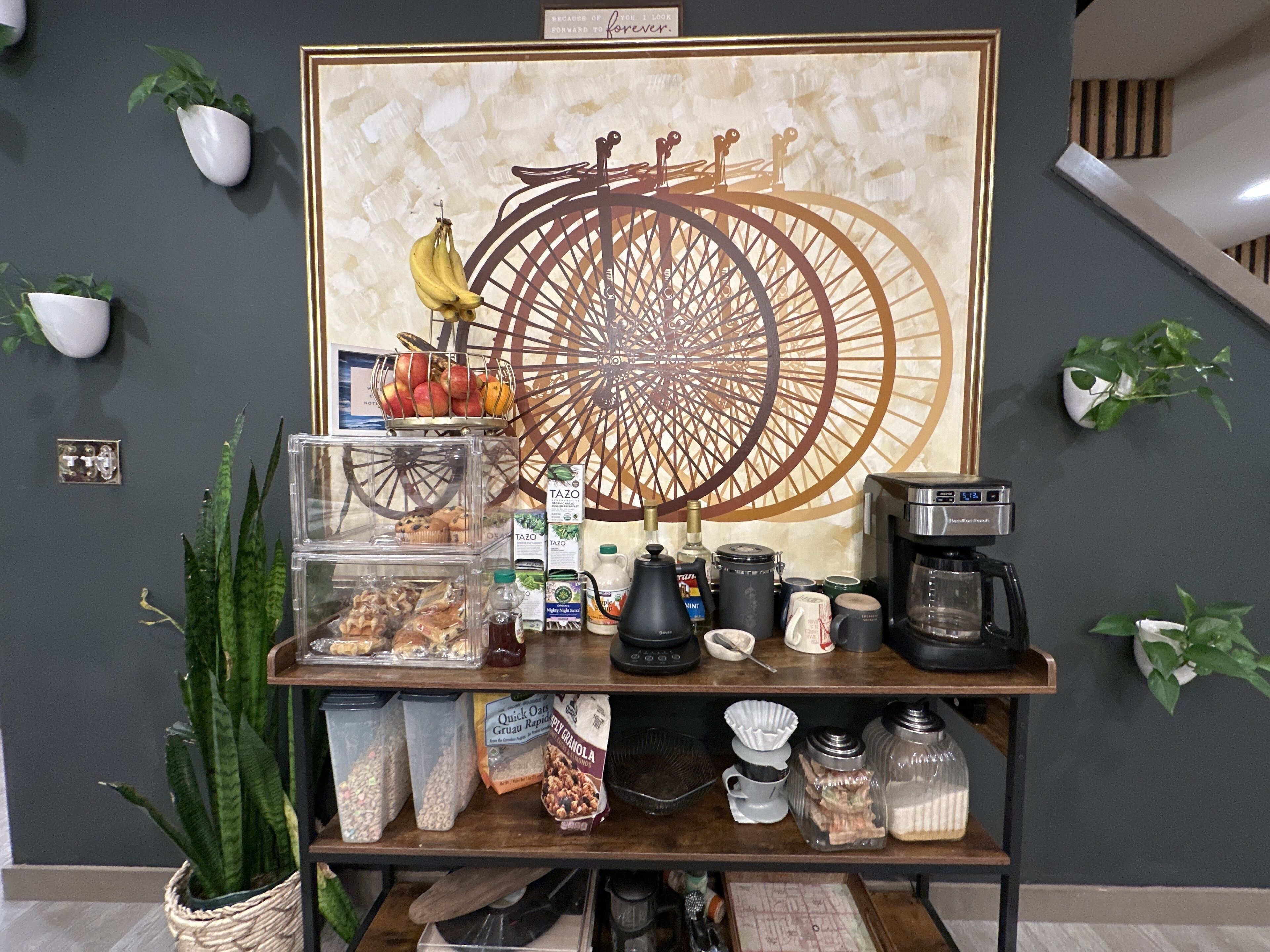 Een koffiehoek met een ontwerp geïnspireerd op een vintage fietswiel, een koffieapparaat en diverse etenswaren.