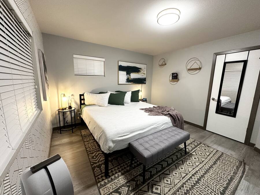 A bedroom with a bed, bedside tables, a bench, a rug, and a door.