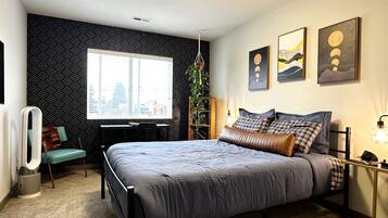 A modern bedroom with a large bed, a desk, and a chair. There is a window with a city view, and the room has a black and white patterned wall.