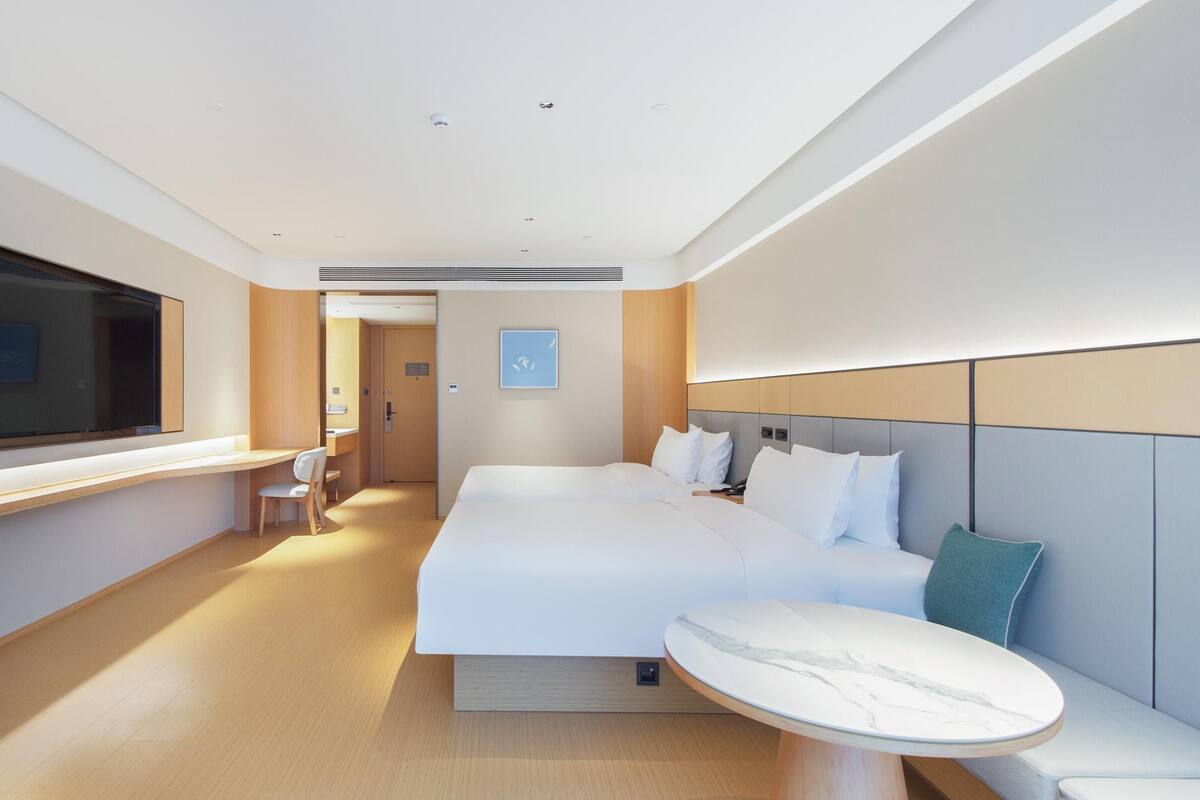 A modern hotel room with a large bed, bedside table, and a seating area with a view of the hallway.