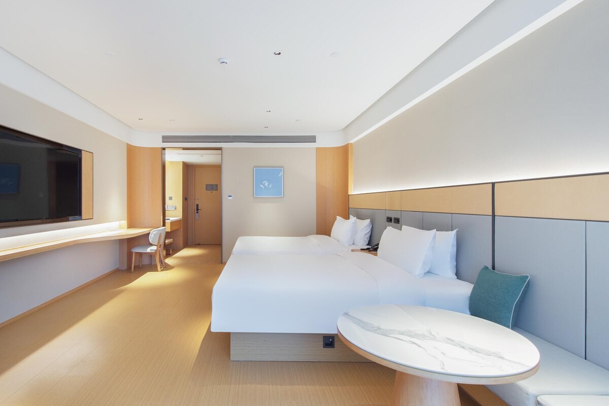 Ett modernt hotellrum med en stor säng, ett nattduksbord och en sittgrupp med utsikt över korridoren.