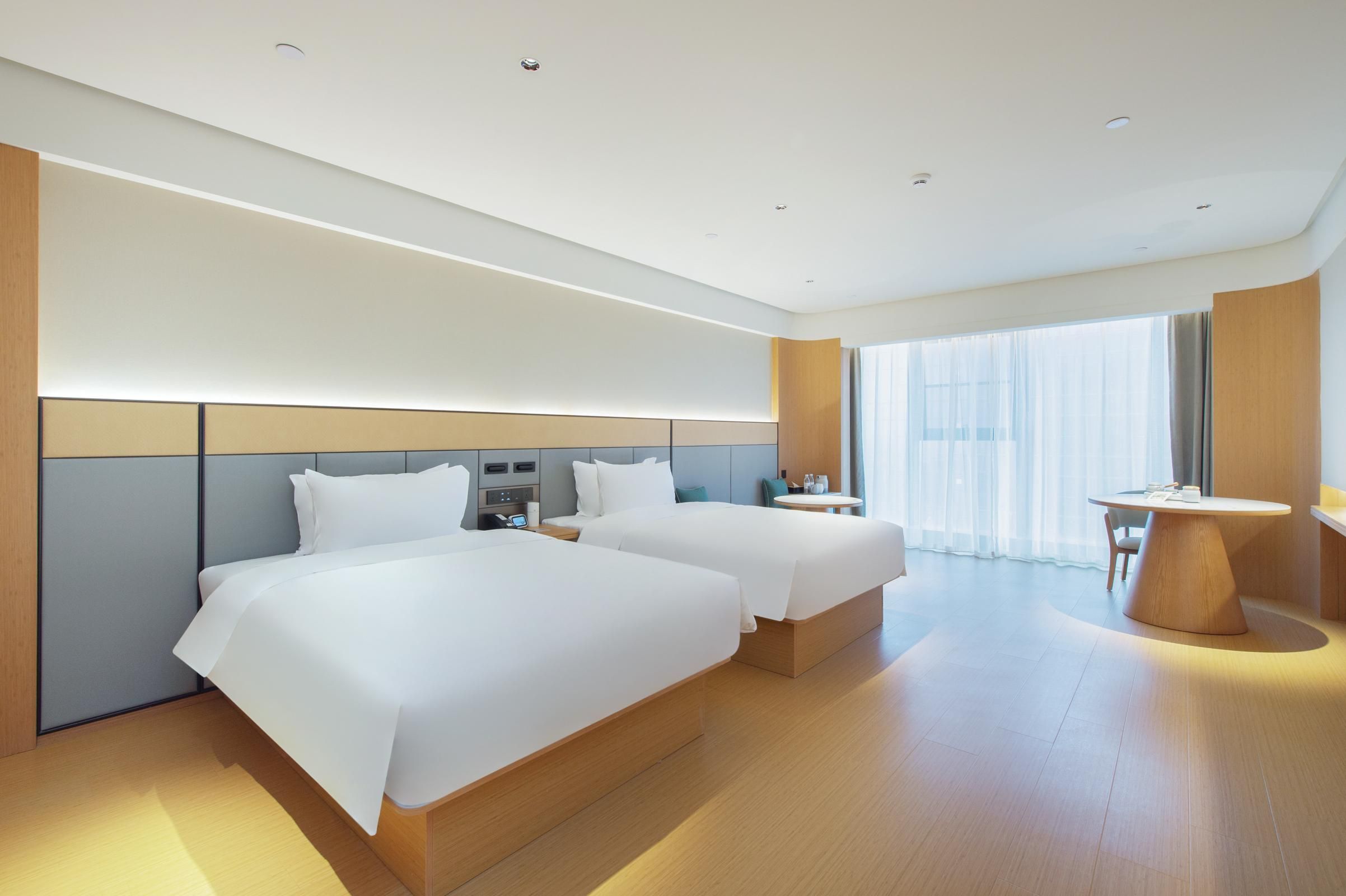 Een moderne hotelkamer met twee bedden, een bureau en een ronde tafel.