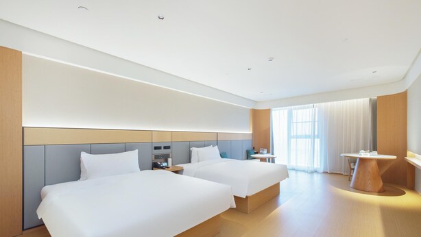 Habitación de hotel con dos camas, un escritorio, una silla y un ventanal con cortinas.