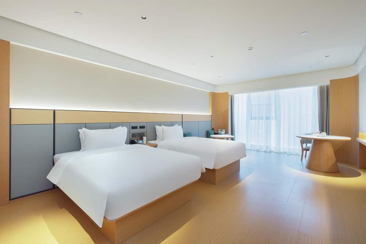 A modern hotel room with two beds, a desk, and a round table.
