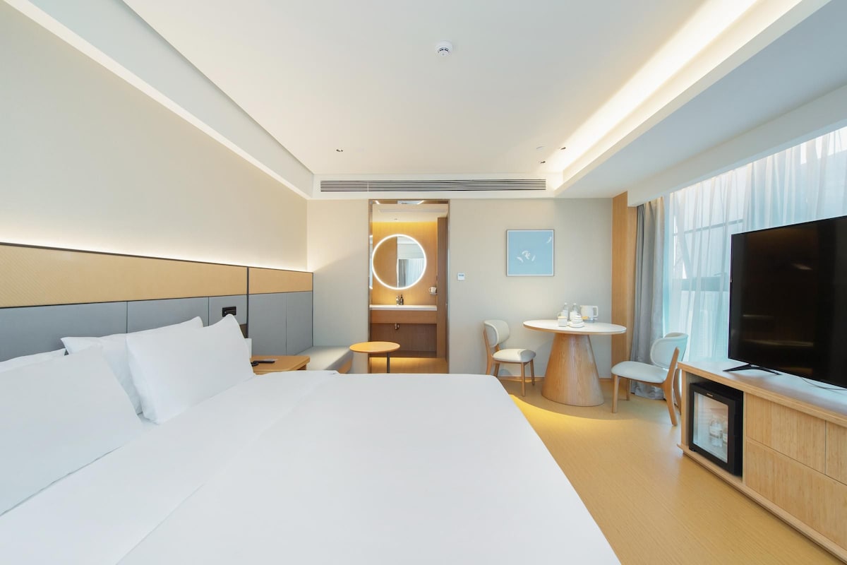 A hotel room with a large bed, a TV, a small table with chairs, and a kitchenette.