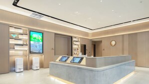 Uma área de recepção com balcão, telas digitais, uma grande tela e um logotipo na parede.