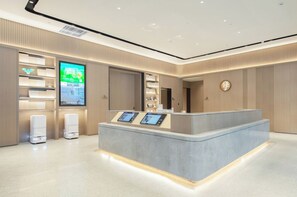 A reception area with a counter, digital displays, a large screen, and a logo on the wall. - Ji Hotel Xiangyang Dongjin Minfa Century Plaza (Xiangyang)