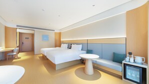Quarto de hotel moderno com uma cama grande, uma pequena mesa redonda, um sofá, uma escrivaninha e um mini-refrigerador.