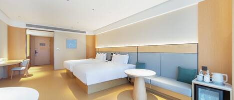 A modern hotel room with a large bed, a small round table, a sofa, a desk, and a mini-fridge.