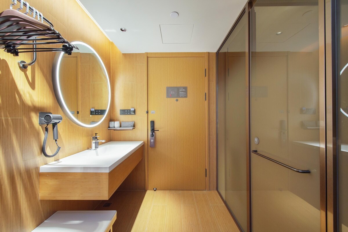 A modern bathroom with a wooden vanity, a mirror with a light, a shower area, and a glass door.